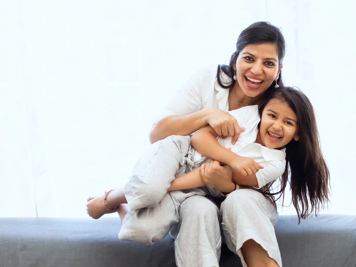 A mother hugging her laughing daughter on a sofa