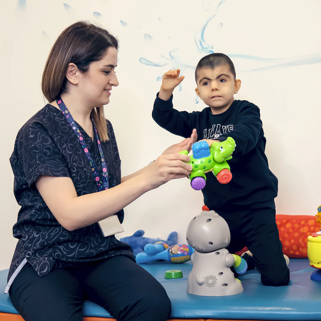 A therapist playing with a smiling young boy and colorful toys during a session
