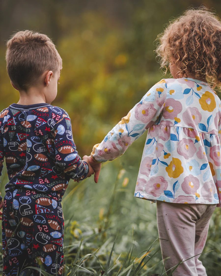 Two young children holding hands as they walk through tall grass